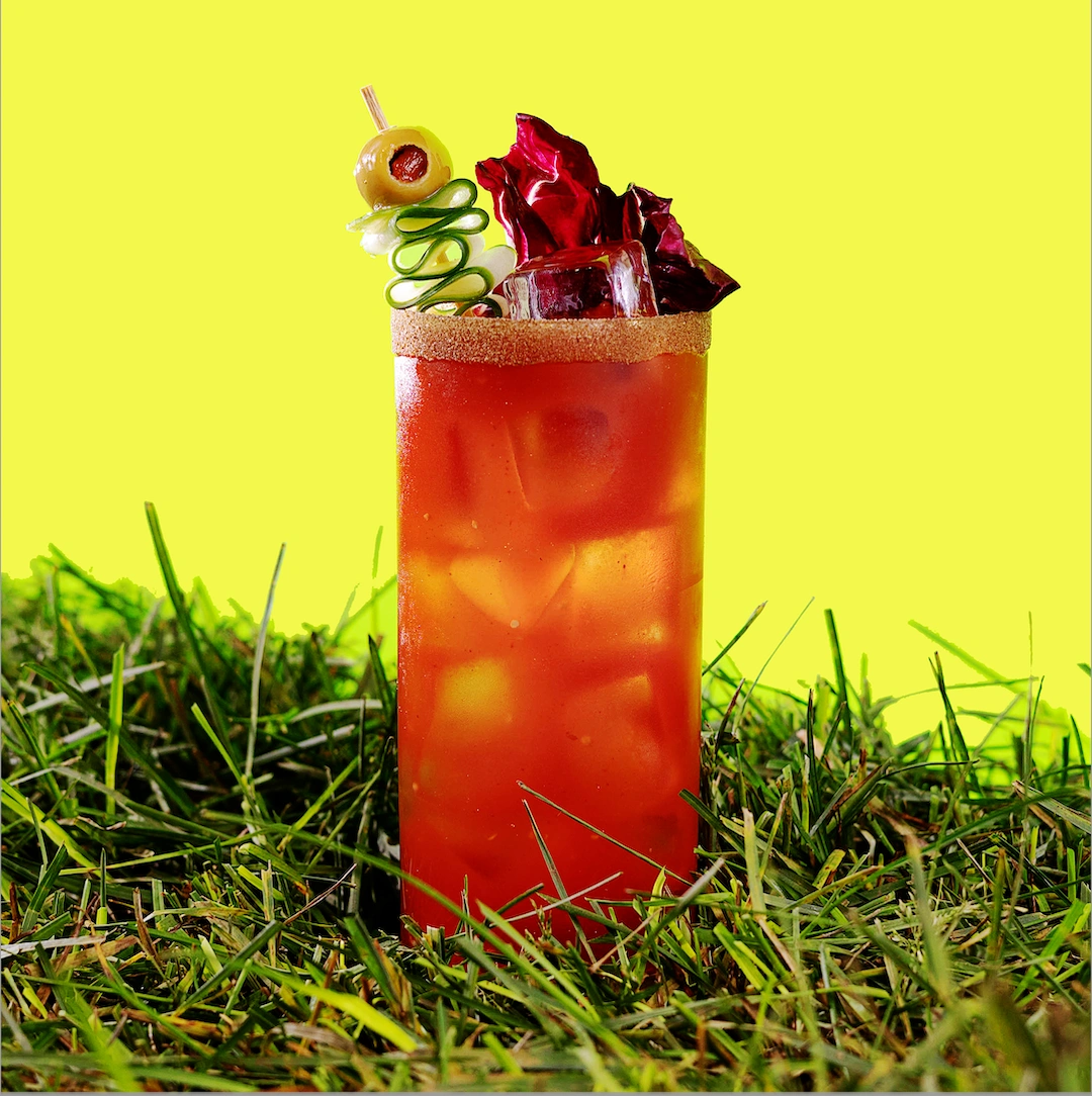 Cocktail à base de gin, de mix à bloody, de clamato, de concombre, de moutard et de sauce aigre-douce sur fond vert pâle.