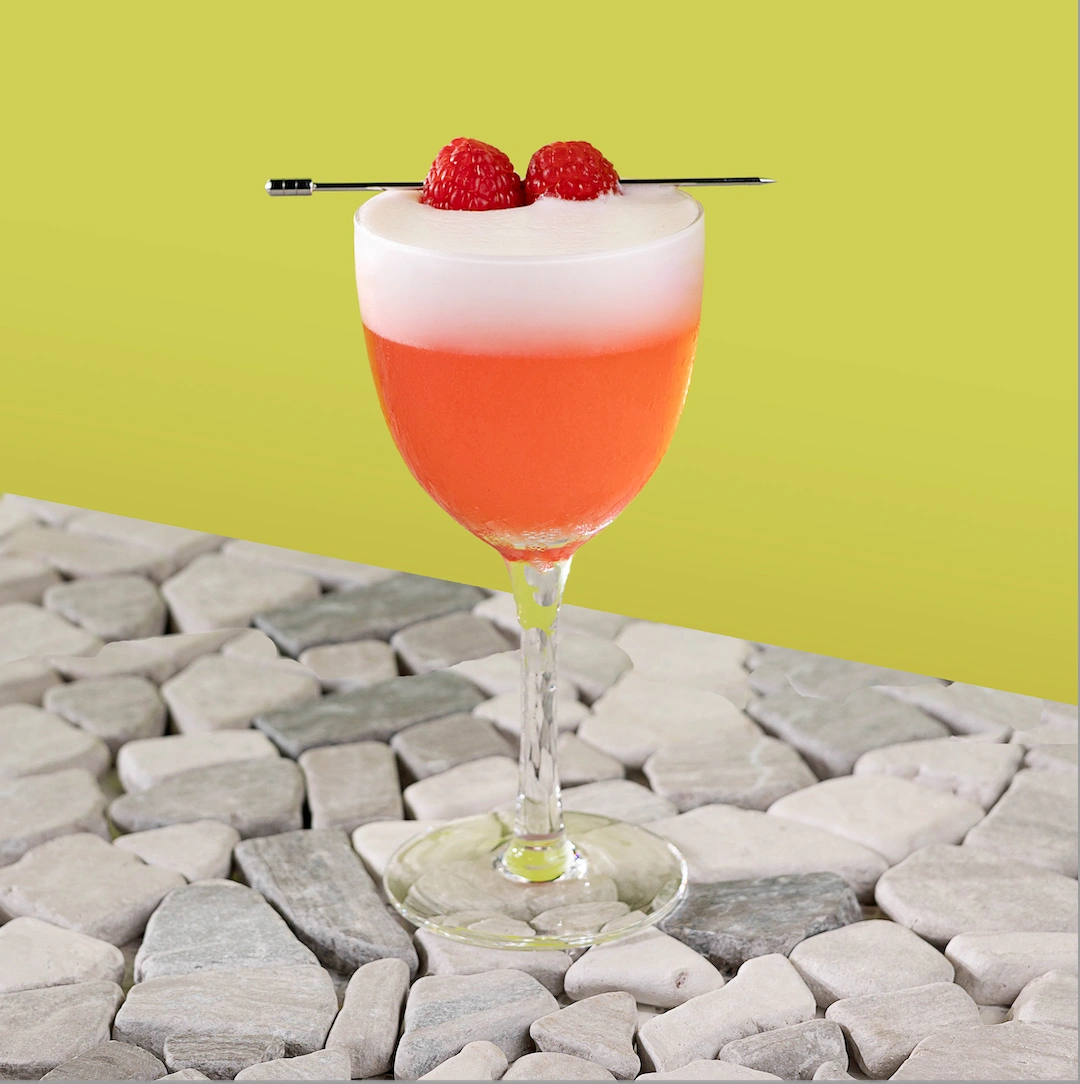 Cocktail made with gin, raspberry syrup, fresh lemon juice and egg white on a green background.