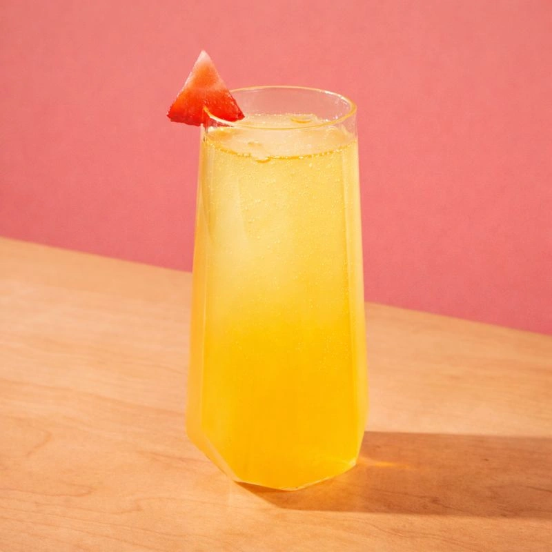 Cocktail à base de mousseux, de sirop de licorne rouge et de jus d'orange frais sur fond bleu.