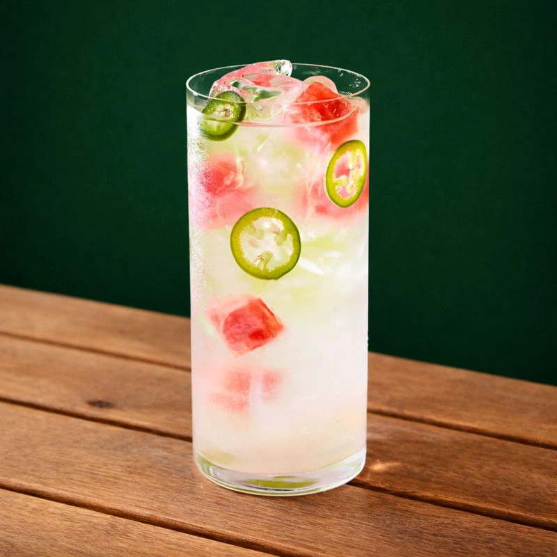 Cocktail à base de sirop de licorne rose, de jus de lime, de melon d'eau, de piment et d'eau glacée sur fond vert.