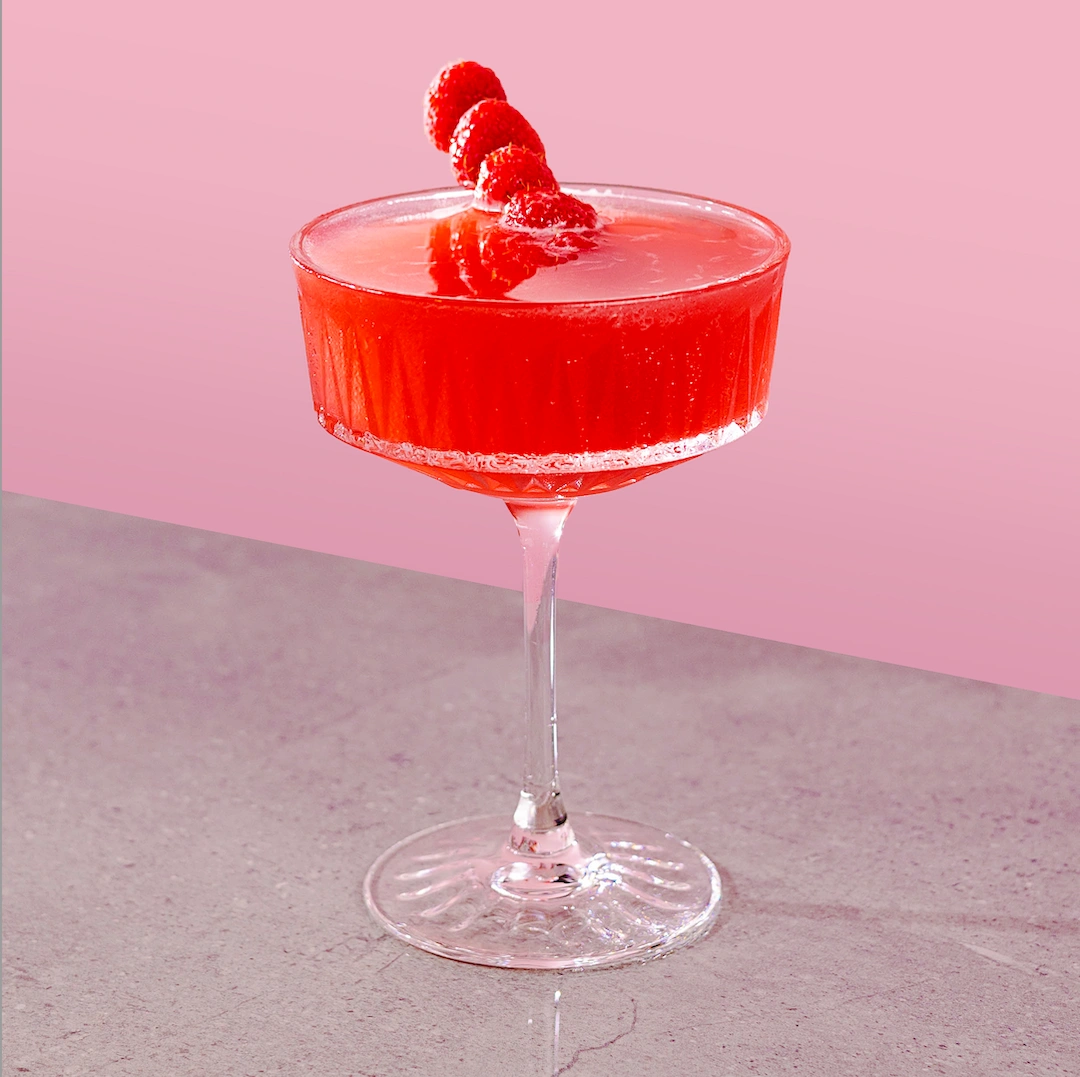 Cocktail à base de rhum blanc, de sirop de framboise et de jus de lime frais sur fond rose.