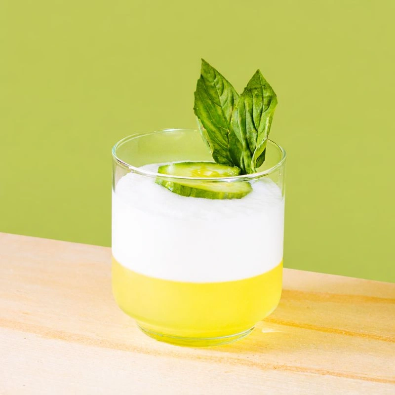 Cocktail made with gin, lime syrup, lemon, cucumber and egg white on a green background.