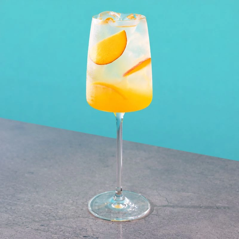 Cocktail made with white wine, peach syrup and lemonade on a blue background.
