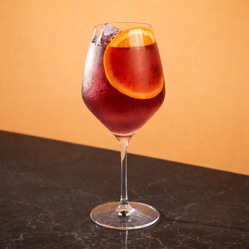 Cocktail à base de vin rouge, de sirop de gingembre et de jus d'orange sur fond lilas.