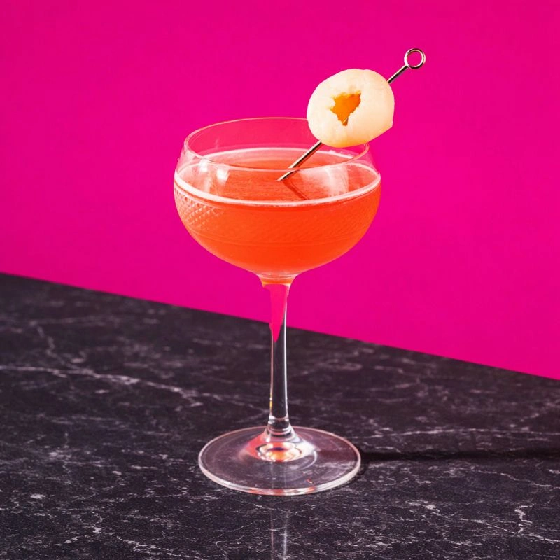 Cocktail made with vodka, lychee syrup and cranberries on a pink background.