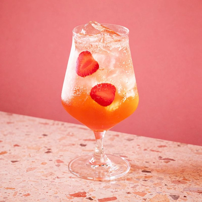 Cocktail à base d'apéritif italien, de sirop de licorne fraise et citron et d'eau pétillante sur fond orange.