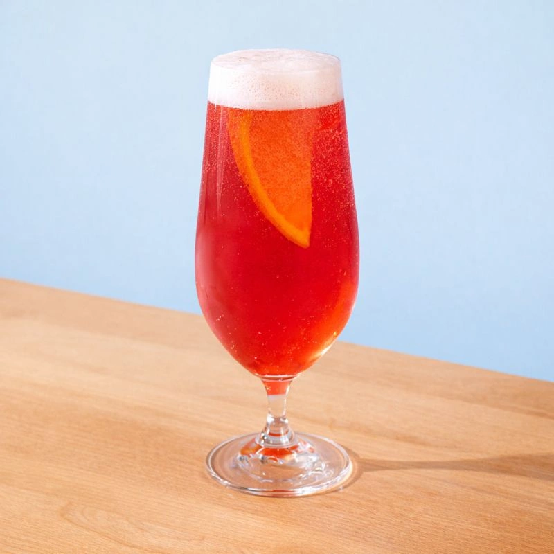 Cocktail made with wheat beer, ginger, and raspberry on an orange background.