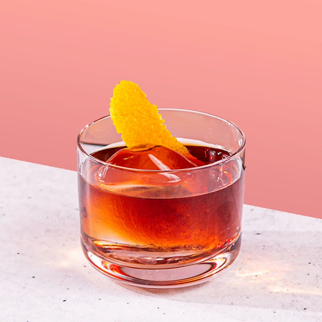 Cocktail made with bourbon, Italian bitters and red vermouth on a salmon pink background.