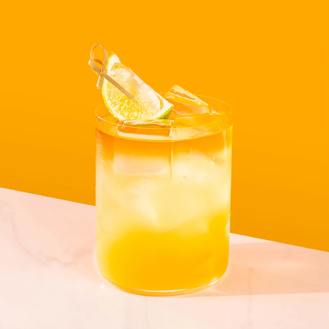 Punch made with rum, orange liqueur, ginger syrup, pineapple juice, lime juice and Angostura on an orange background.