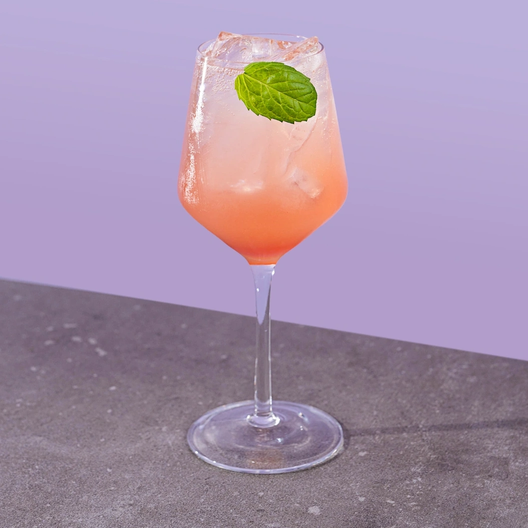 Cocktal made with lager, ginger syrup, red unicorn syrup, cream soda and balsamic vinegar on a mauve background.