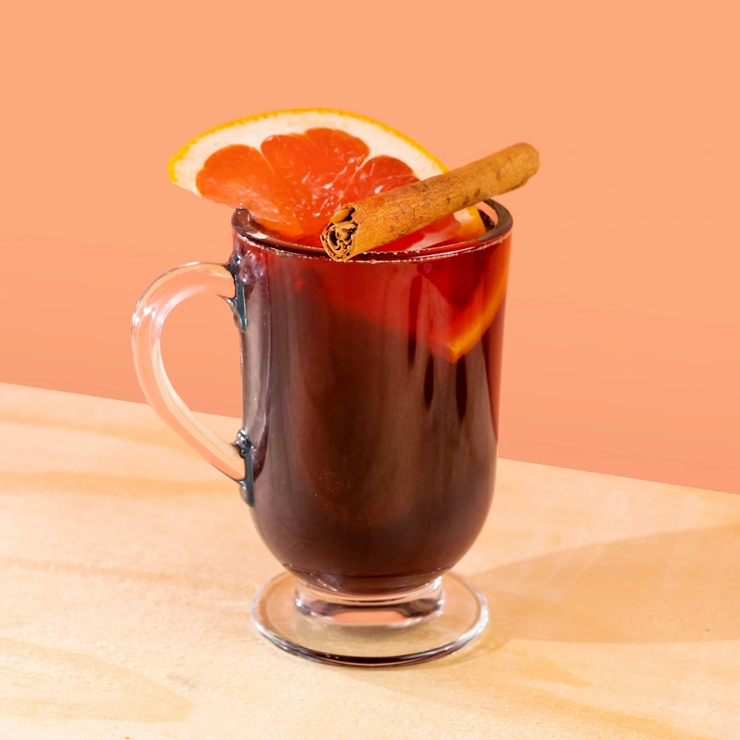 Hot cocktail made with wine, ginger syrup, maple syrup and spices on a pink background.