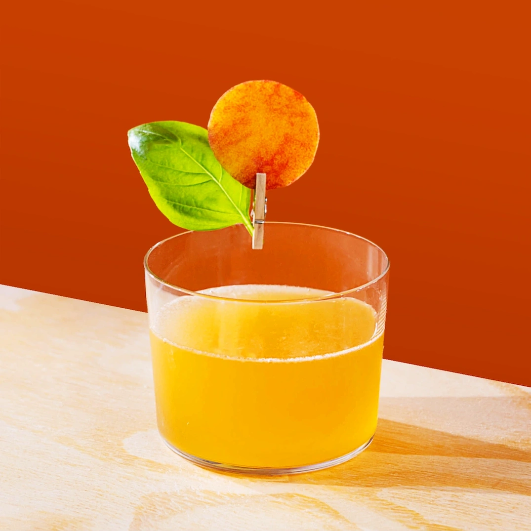 Cocktail made with white rum, peach syrup and fresh lime juice on a burnt orange background.