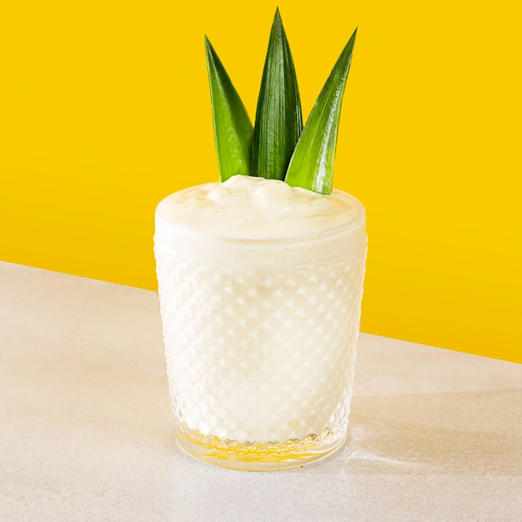 Cocktail à base de rhum, de sirop de lime, de lait de coco et d'ananas sur fond jaune.