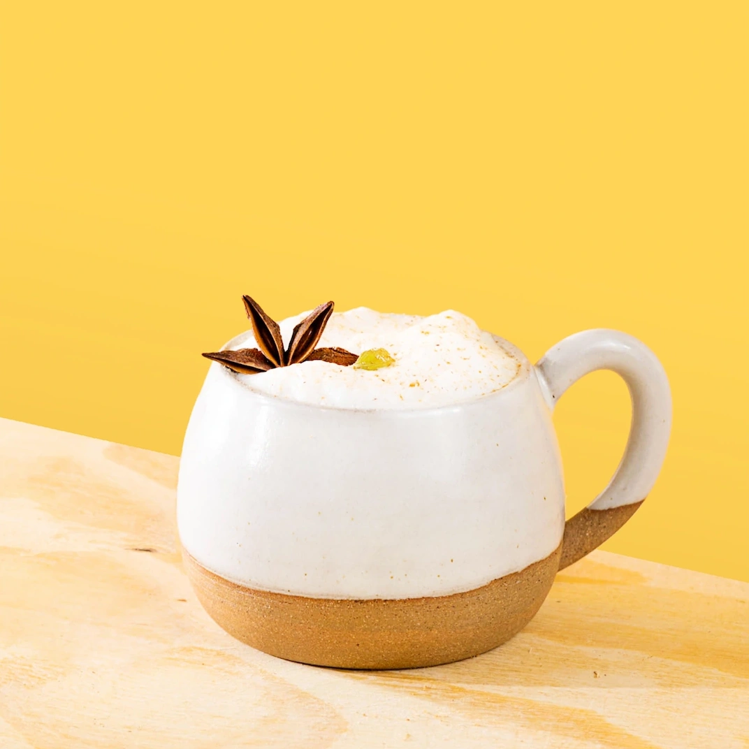 Chai tea made with pumpkin spice syrup, frothed milk and spices on a yellow background.