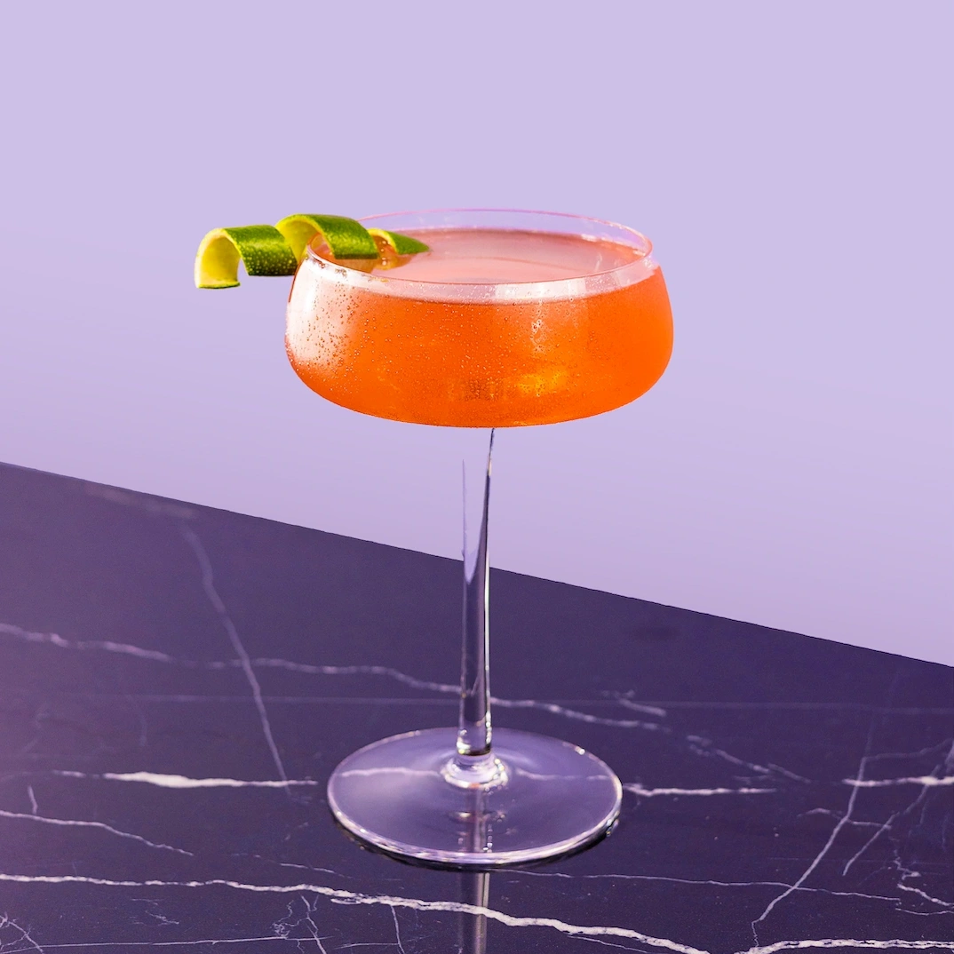 Cocktail made with vodka, lime juice and grenadine on a lilac background.