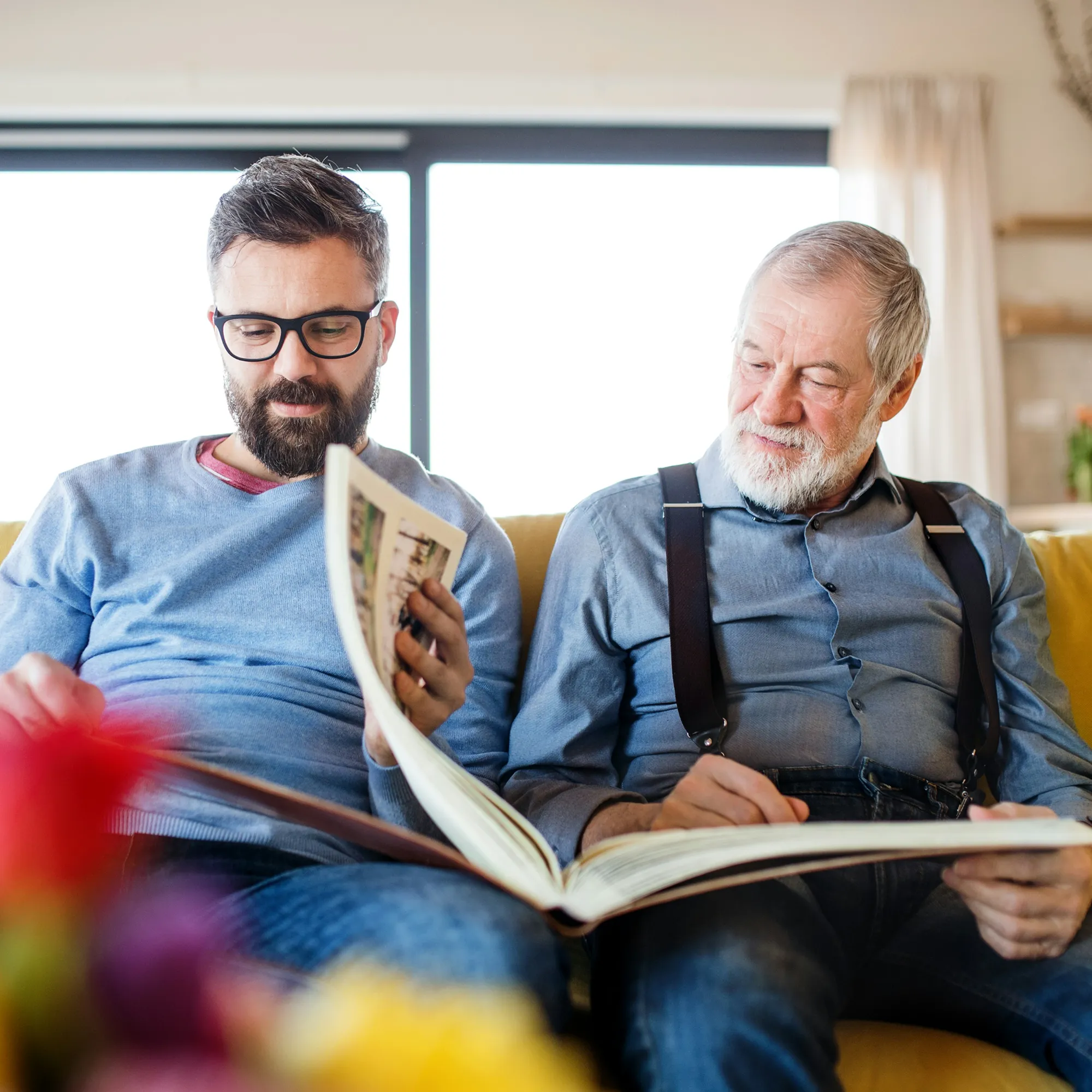 Older man and younger man sitting on a couch looking at a large photo album together.