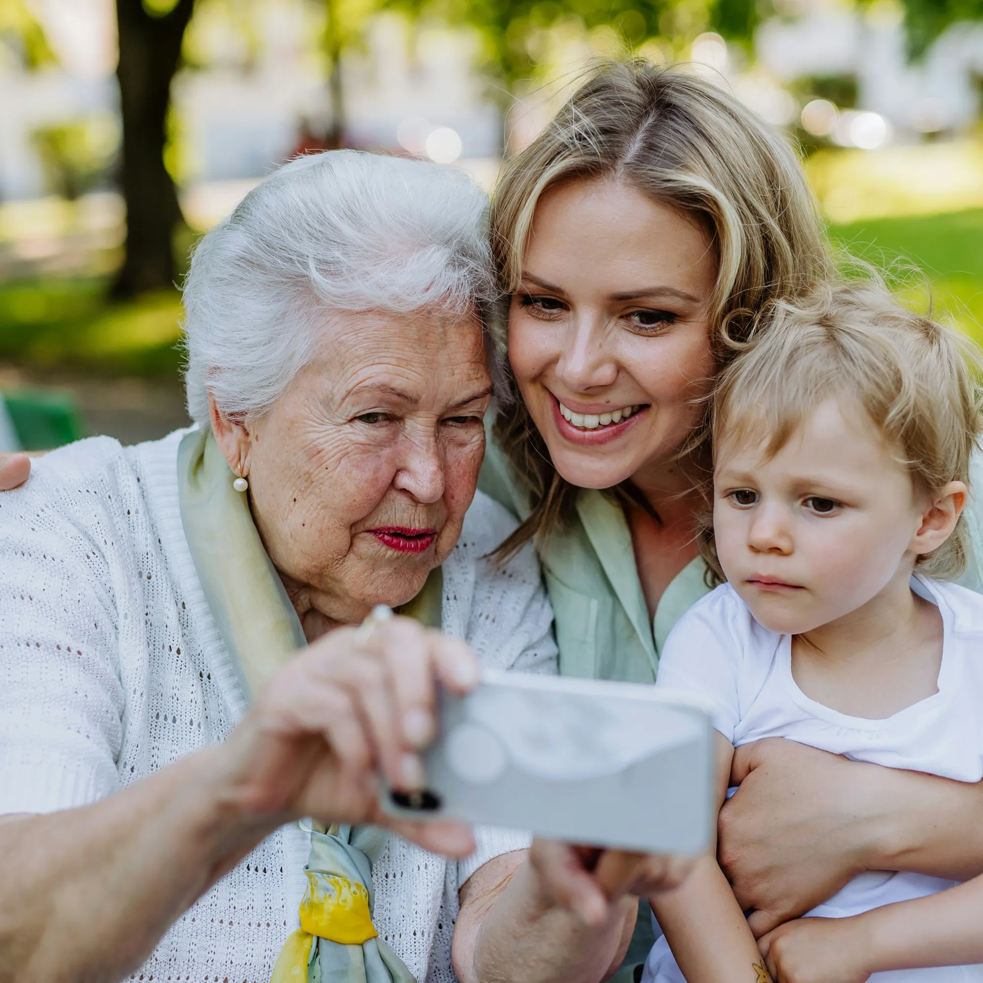 Elderly woman, middle-aged woman, and young child taking a selfie together outdoors.