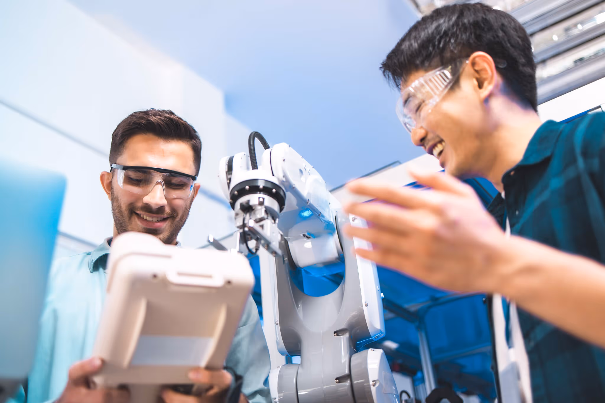 Two male engineers wearing safety glasses working with a robotic arm in a lab.