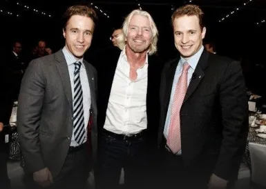 Three men in suits posing together at an indoor event with string lights in the background.