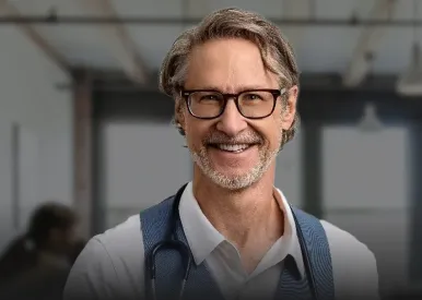 Smiling middle-aged male doctor with glasses and stethoscope in a bright room.