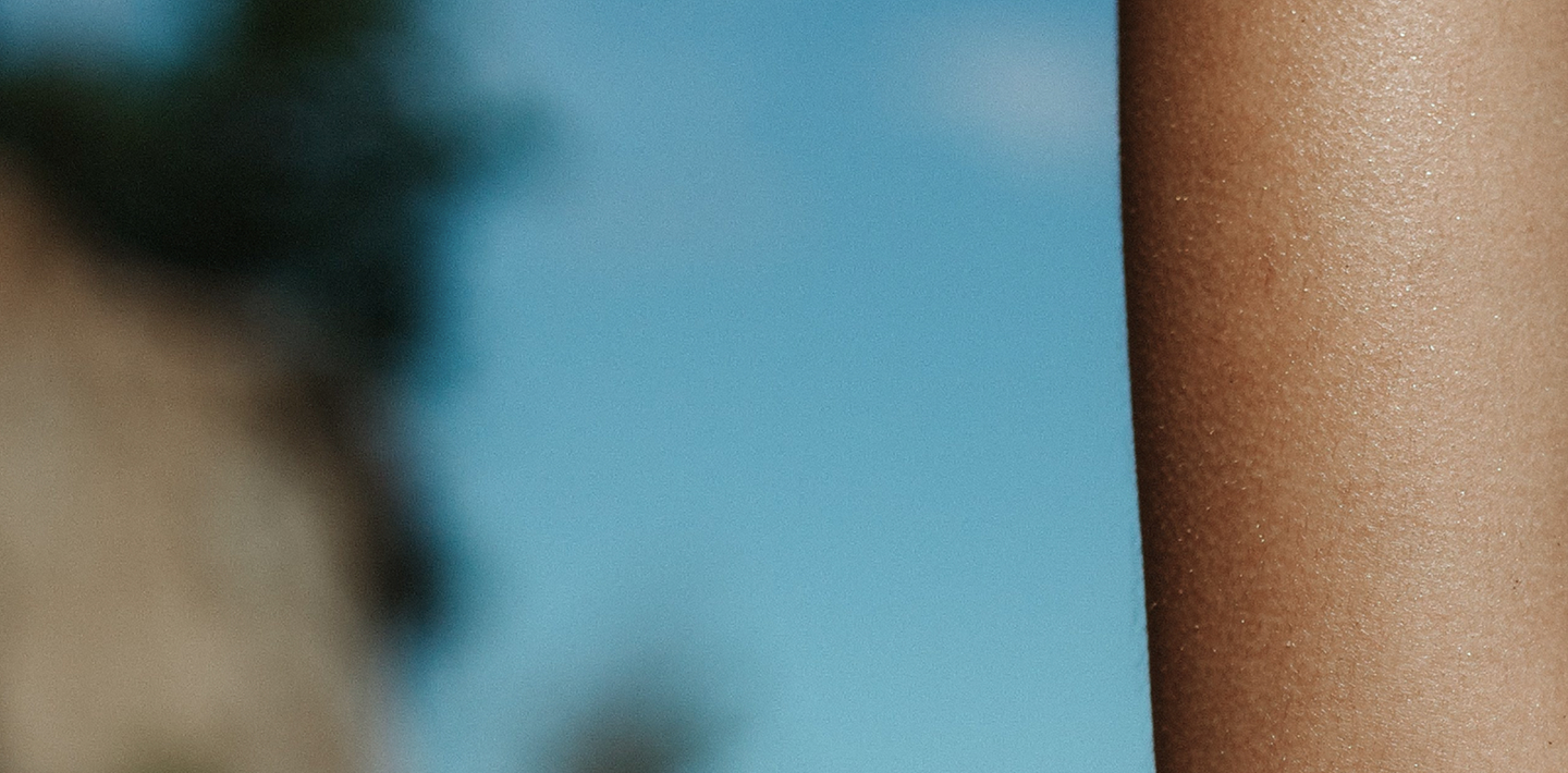 A woman's arm close-up, with beach and sky in background.