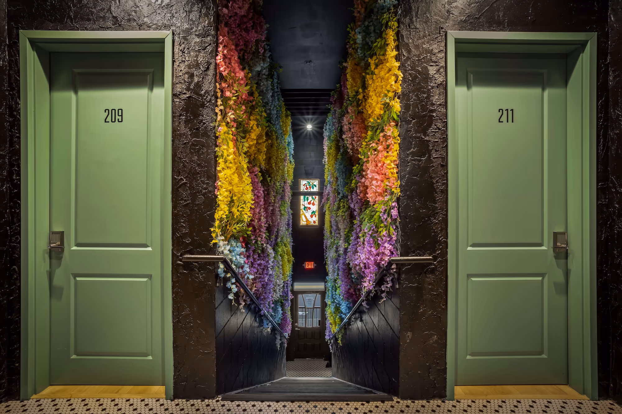 Staircase descending between walls covered with colorful floral decorations, flanked by green doors numbered 209 and 211.