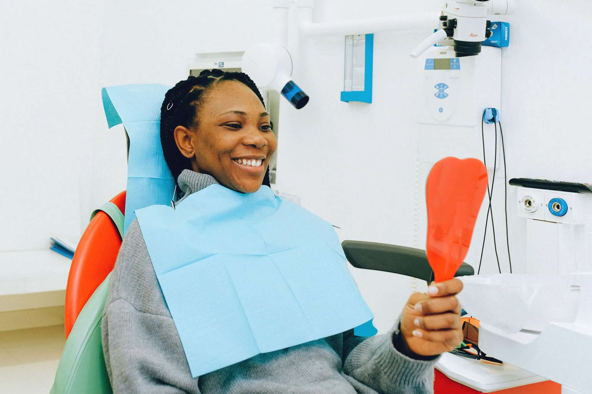 Smiling patient in a dental chair admiring her new smile in a hand mirror