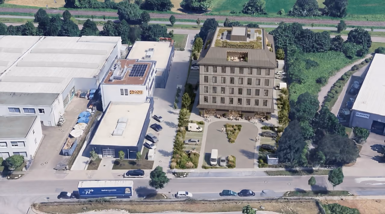 Luftaufnahme von Gewerbegebäude mit Parkplätzen und LKW auf der Straße davor.