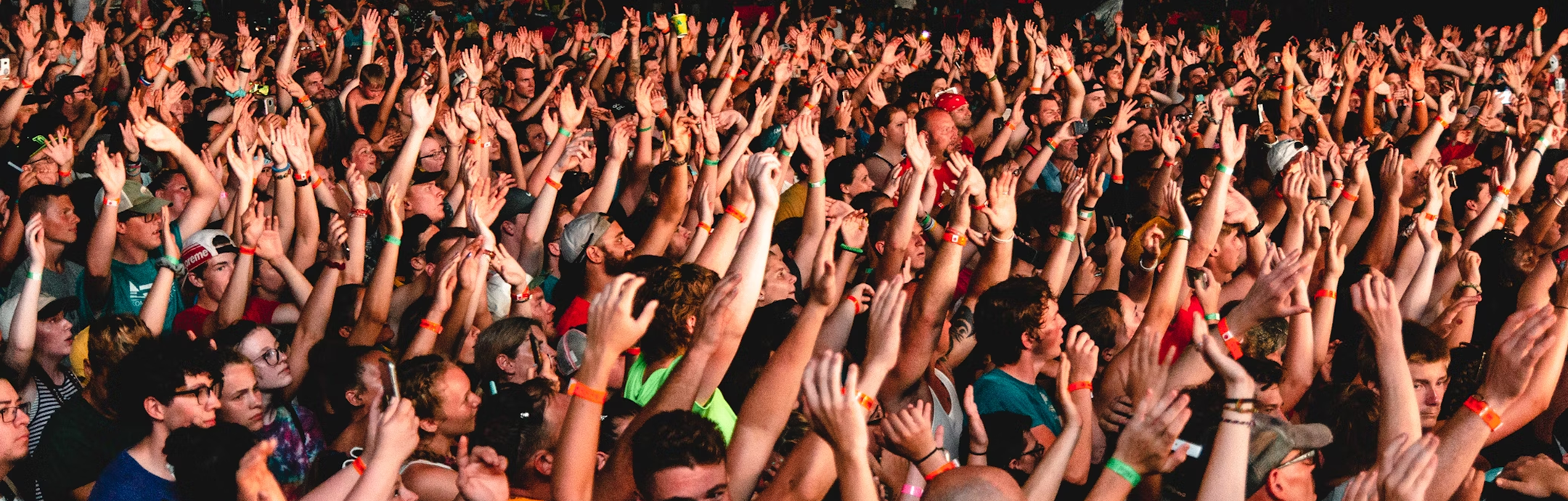 Large crowd of people at a concert or event raising their hands in the air.
