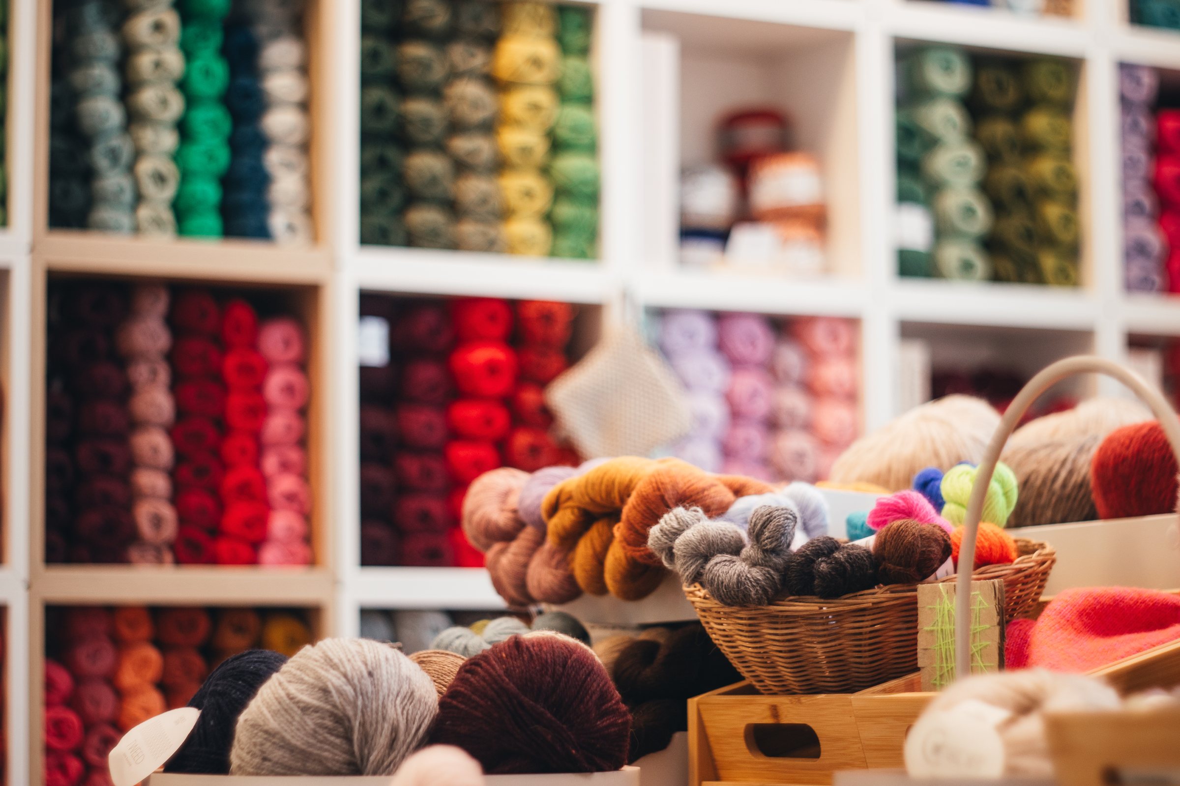 Regal mit bunten Garnsträngen und Wollkörben im Strickladen
