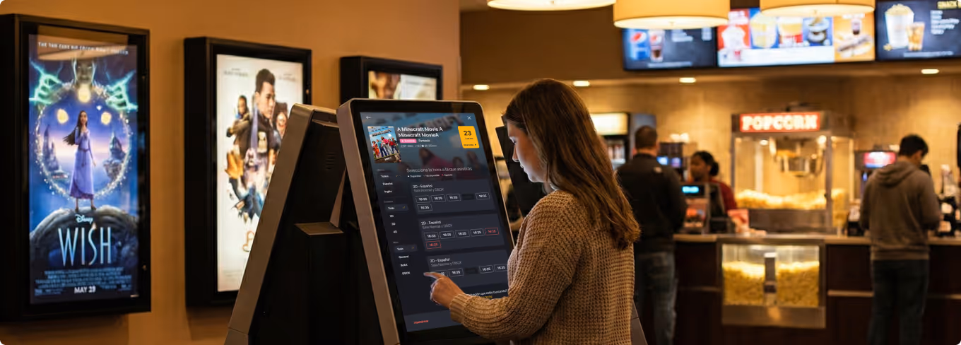 Mujer usando un kiosco digital para seleccionar boletos de cine en el lobby.