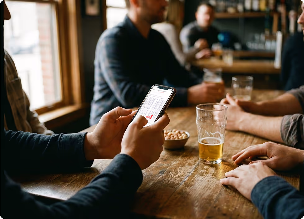 Hombre sentado junto a sus amigos selecciona sientes para un partido de futbol por medio de su celular.