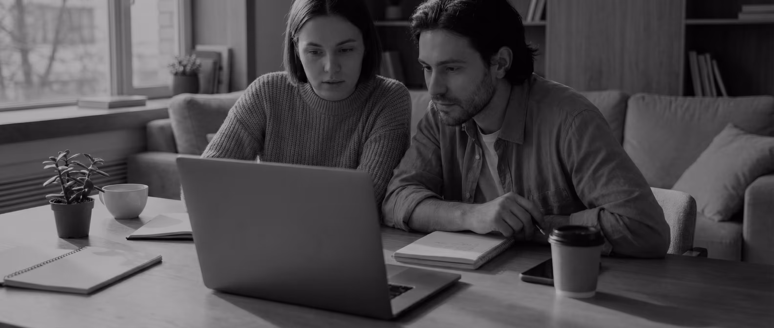 Una pareja sentada en un sofa en la sala de su casa mientras observan en una computadora portátil el estado de su cuenta bancaria.