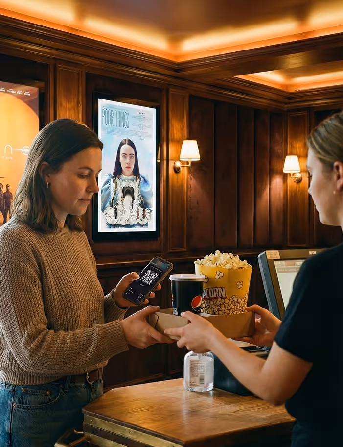 Woman scanning a QR code on her phone while receiving popcorn and a drink from a cashier at a movie theater counter.