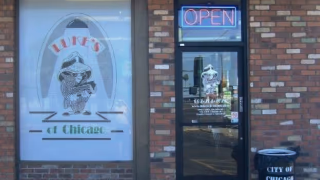 Brick storefront with a glass door displaying a neon 'OPEN' sign and a window featuring a logo of a character in a sombrero with text 'LUPE'S at Chicago.'