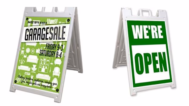 Two white A-frame signs: left sign advertises a garage sale with green background and times Friday 9-3, Saturday 8-4; right sign says WE'RE OPEN in white text on green background.