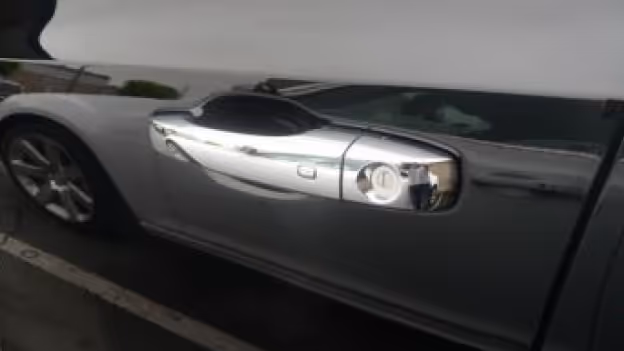 Close-up of a shiny chrome car door handle on a silver vehicle.