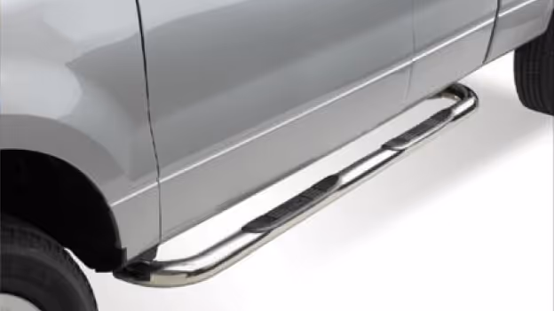 Chrome step bar with black non-slip pads installed along the side of a silver pickup truck.