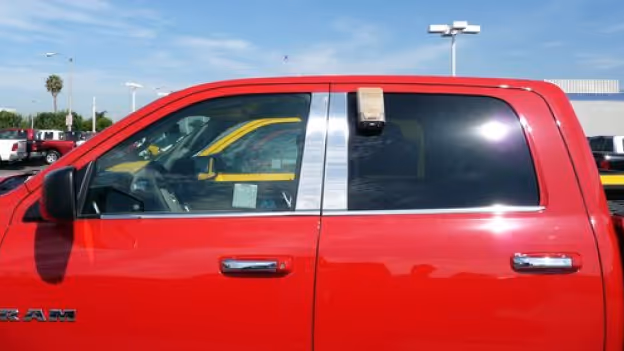 Side view of a red pickup truck with stainless steel pillar post trim between the front and rear windows.
