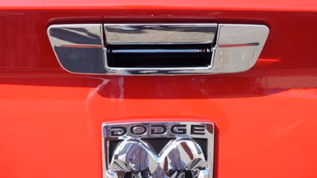 Close-up of a red Dodge tailgate showing a chrome handle and the Dodge emblem with ram's head logo.
