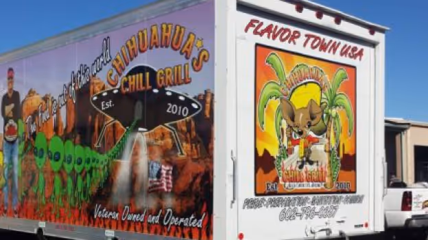 Food truck with vibrant artwork advertising Chihuahua's Chili Grill, featuring green aliens on the side and a desert sunset with a chihuahua mascot on the back.