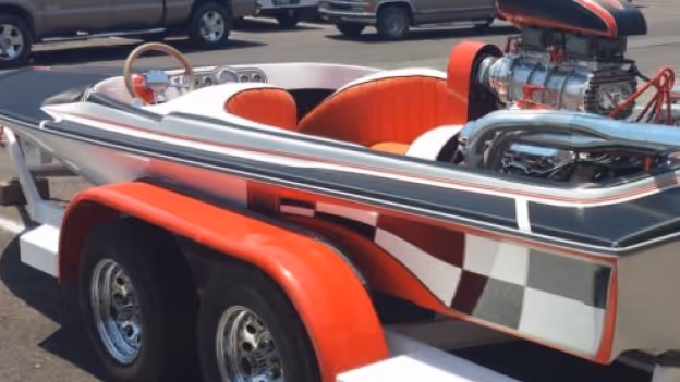 Close-up of a custom shiny boat with red and white interior seating, chrome details, and a large engine on a red and white trailer.