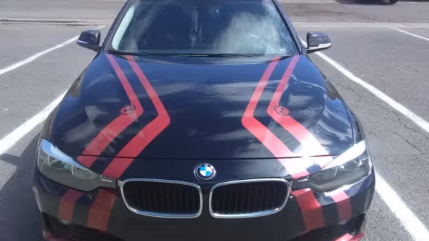Front view of a black BMW car with red racing stripes parked between white lines.