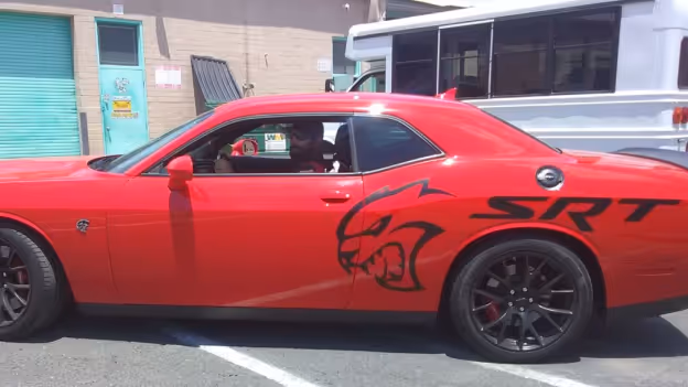 Red Dodge Challenger SRT with a black fierce cat graphic on the side, parked in a lot near a building and white truck.