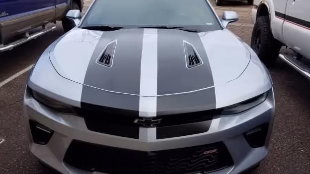 Front view of a silver Chevrolet Camaro with black and white racing stripes on the hood.