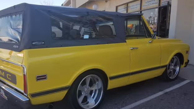Yellow vintage GMC SUV with a black soft top parked in a parking lot near a building.