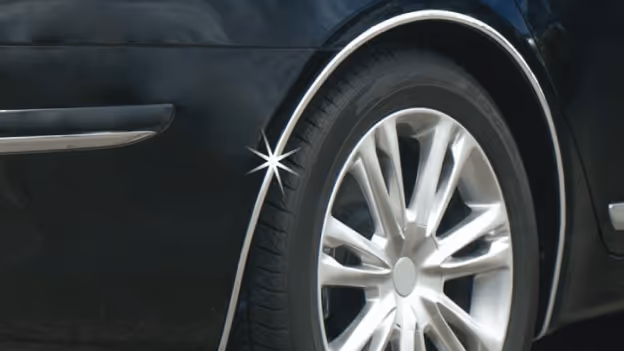 Close-up of a car's rear wheel with a shiny chrome wheel arch molding on a black vehicle.