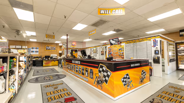 Interior of a racing-themed sales counter with bright yellow and black decor and signs reading 'Will Call' and 'Sales Counter.'