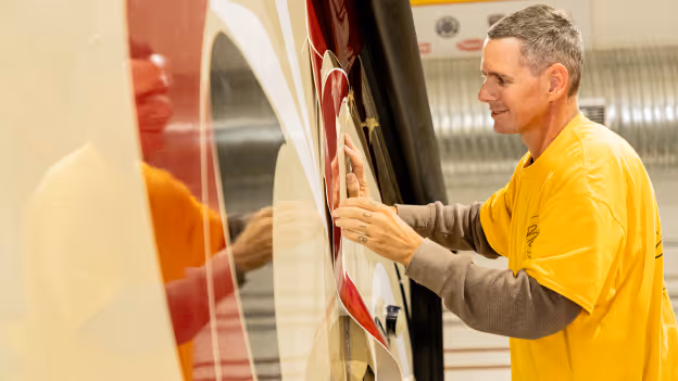 Man in a yellow shirt applying red and white vinyl wrap to the side of a vehicle.