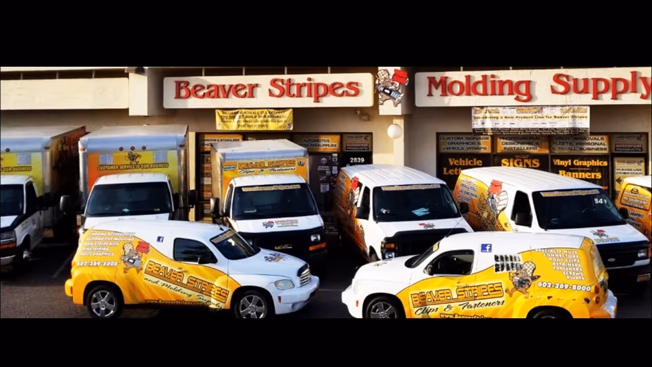 Fleet of Beaver Stripes branded vehicles parked in front of a Beaver Stripes Molding Supply storefront.